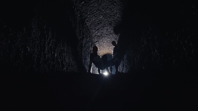 In the depths of a dark cave, the backlit silhouettes of a group perform a solemn ritual around a figure lying on the ground. The scene is mysterious, spiritual, and full of unspoken drama.