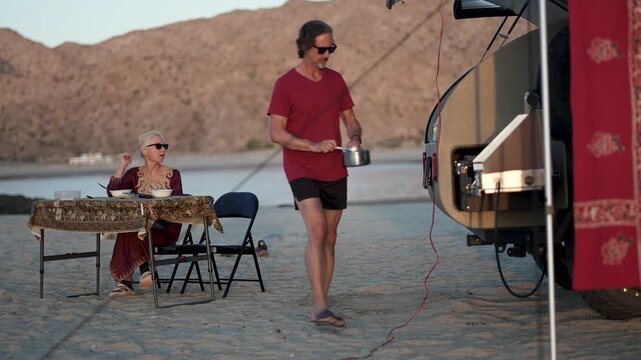 Mature man and woman dine together as the sun sets near their camper on a beach in Baja California, Mexico.