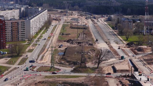 Aerial view in Riga, Latvia shows Southern Bridge phase four, Riga TV Tower, forest band, Soviet era block, roadbeds excavate and pave, cranes, trucks, rollers.