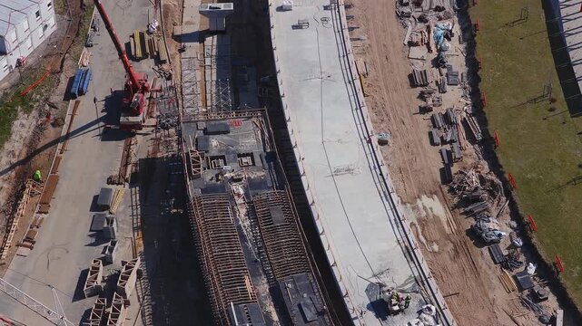 Aerial top down view of Southern Bridge phase 4 in Riga, Latvia. Cranes lift materials, crews finish concrete, rebar and shuttering set, machinery and formwork visible.
