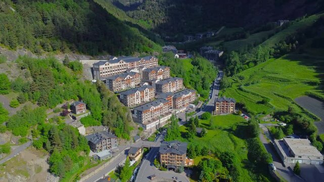 aerial perspective captures a picturesque mountain valley in Andorra, showcasing residential buildings nestled amidst lush green slopes and winding roads, highlighting the serene beauty and unique arc