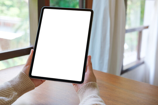 Mockup image of a woman holding digital tablet with blank white desktop screen at home