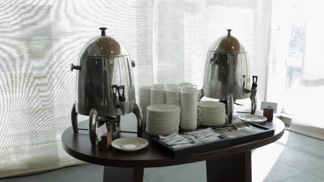 Self-service coffee and tea station with two stainless steel urns, white cups, and sugar sachets for a business conference break.