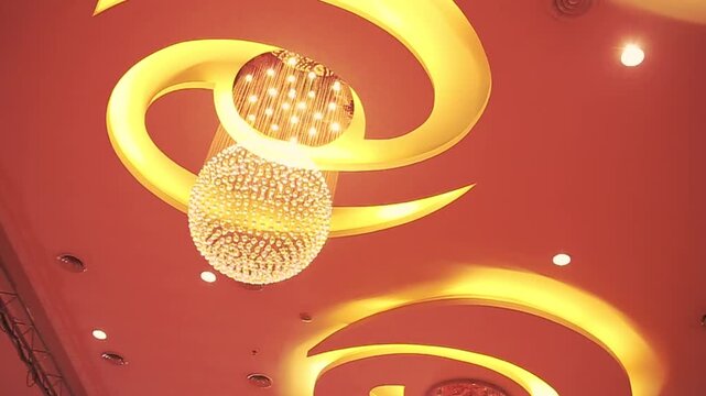 Modern architectural ceiling design with curved cove lighting and a luxurious crystal sphere chandelier in a grand ballroom.