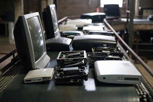 Old computer monitors and disassembled electronics on a conveyor belt in a recycling facility