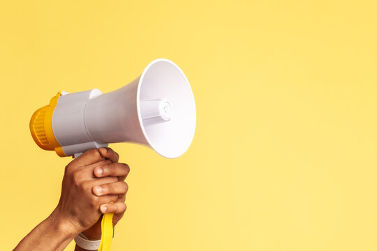 Portrait of bearded handyman wearing blue overalls and red cap screaming announcing about discounts of service industry or protesting. Indoor studio shot isolated on yellow background.