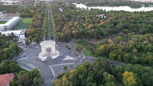 Aerial drone footage of the historic Arch of Triumph (Arcul de Triumf) in Bucharest, Romania. Landmark monument inspired by the Parisian arc, surrounded by traffic and spring greenery.