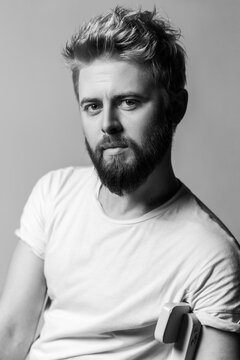 Black and white shot of calm attractive man with beard posing for portrait looking at camera with healthy skin isolated on gray background