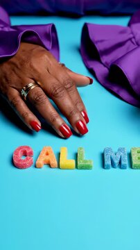 Creative hands display colorful letters on blue background. Woman's hands show message 'Call Me' with vibrant candies. Bright colors create playful atmosphere. Vertical orientation enhances visual