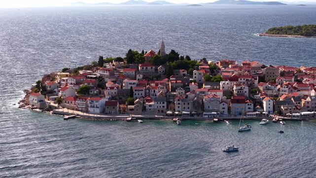Aerial view of the historic town of Primosten on a peninsula in the Adriatic Sea, Croatia, featuring traditional red-roofed houses and a church steeple on a sunny day