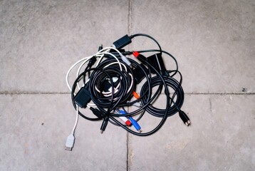 Messy tangle of various electronic cables and connectors on a concrete floor background