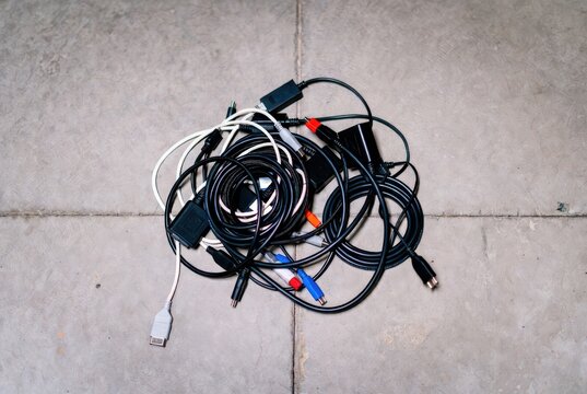Messy tangle of various electronic cables and connectors on a concrete floor background