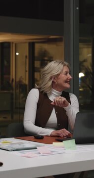 Business, woman and meeting with laptop at night for discussion, training and finance report. Mature person, talking and pc for briefing, coaching pitch and feedback for investment deadline in office