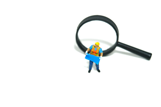 Miniature people toy figure photography. Project location concept. A construction worker with blueprint building standing with compass. Isolated on white background