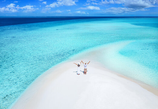Aerial view of a happy couple standing on a sandbank beach with turquoise, clear water in the Maldives islands