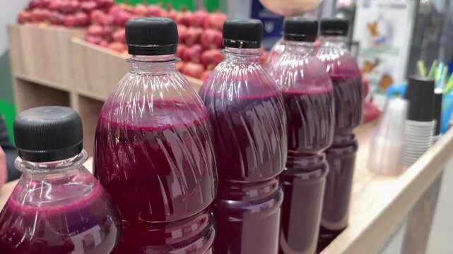 Row of clear plastic bottles filled with freshly squeezed Azerbaijani pomegranate juice on wooden counter at market stall, deep