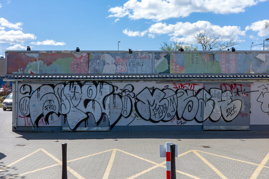 Warsaw, Poland - April 23, 2026: An outdoor wall of a commercial building covered in bold black and silver graffiti throw-ups under a bright blue sky.