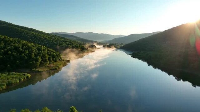 Tranquil aerial view of a lake valley at sunrise with a fog, surrounded by green lush mountains