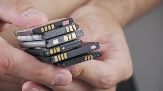 Close-up of male hands holding a pile of old discarded lithium polymer batteries. The macro view emphasizes the environmental danger of hazardous electronic waste.
