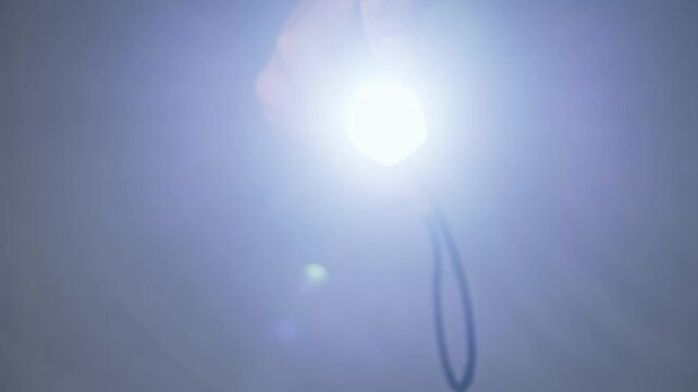 Close-up of a hand holding a black LED torch turning it on and off. The bright beam points directly into the camera lens creating a blinding flash and flare effect.
