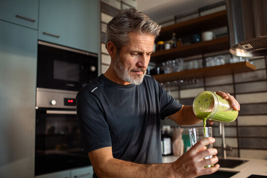 Middle-aged man pouring green smoothie in home kitchen