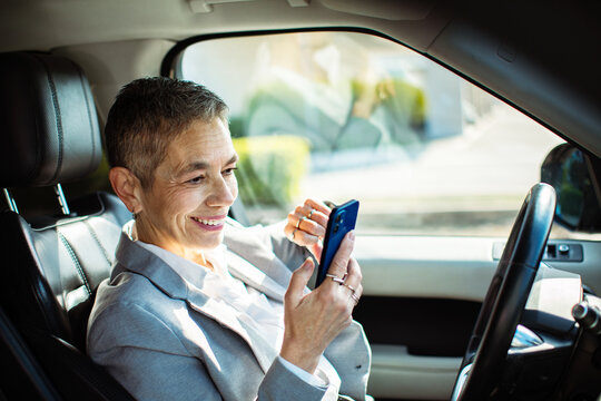Smiling business professional using smartphone in parked car