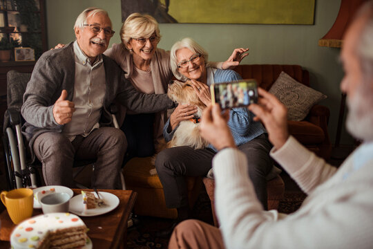 Senior friends posing with dog for smartphone photo at home