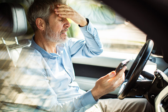 Stressed mature driver holding smartphone in car
