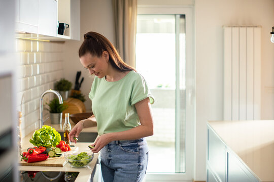 Young woman preparing fresh salad in home kitchen