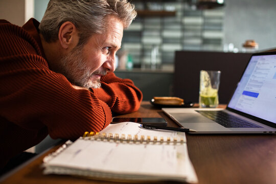 Senior man checking email on laptop at home kitchen table