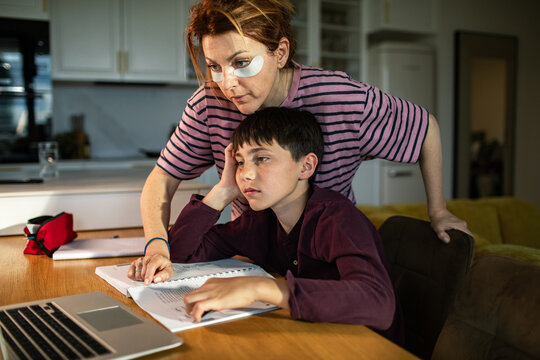 Tired mother helping son with homework at kitchen table
