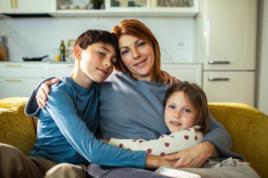 Mother hugging son and daughter on sofa at home