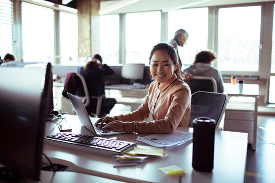 Smiling businesswoman working on laptop in modern open plan office