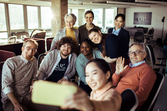 Diverse coworkers taking group selfie in modern office