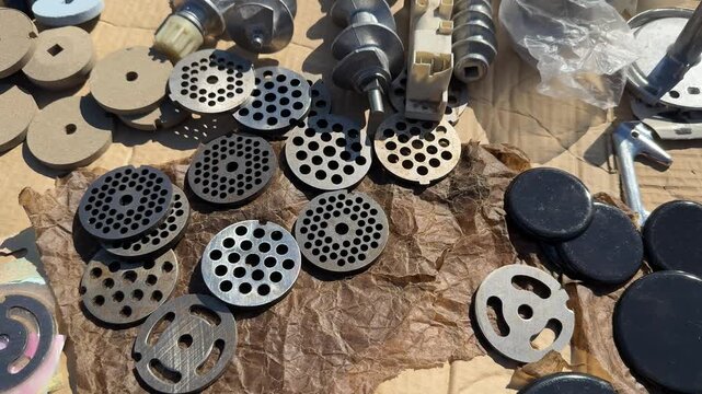 Assorted metal and plastic grinder nozzles laid out on wooden workbench with milling cutter bits round perforated plates dies