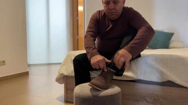 Hombre sentado en la cama terminando de vestirse y calzarse