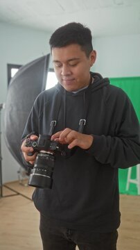 Man photographer holding camera and adjusting lens with hands in a studio, checking settings and dials; concentration practice.