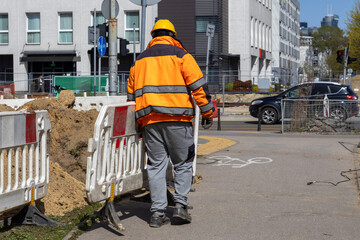 Fototapeta premium A construction worker in a high visibility jacket and safety helmet at a road site manages protective barriers to ensure public safety and organized urban infrastructure during maintenance work