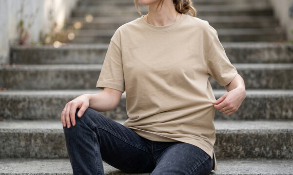 Model Seated on Steps Wearing Plain Oversized Sand Beige Longline T-Shirt Mockup