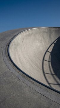 Empty Concrete Skate Park Bowl with Metal Coping Under Clear Blue Sky and Minimalist Shadow