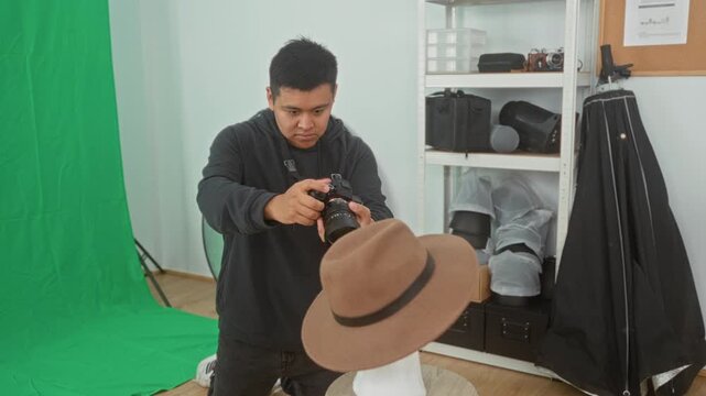Man holding camera adjusting lens in studio by a green backdrop and shelves of gear; creative concentration.