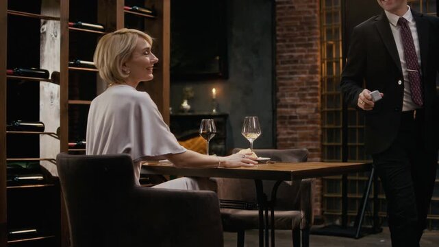 Stab shot of middle-aged Caucasian man in formalwear kneeling and presenting engagement ring during romantic restaurant dinner, proposing marriage to happy elegant woman saying yes