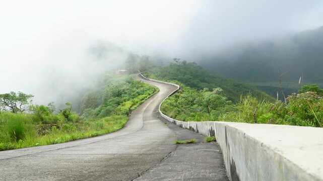Handheld low angle from a concrete barrier showing a winding road enveloped in thick fog leading up to Mount Kelud crater peak in Kediri, East Java, Indonesia, southeast Asia.