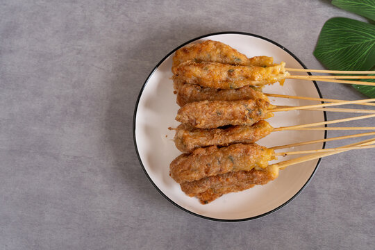 Sempol ayam skewers served on a plate with spicy chili sauce on dark background. Sempol made from chicken, spices and eggs. Popular Indonesian street food snack. Top view