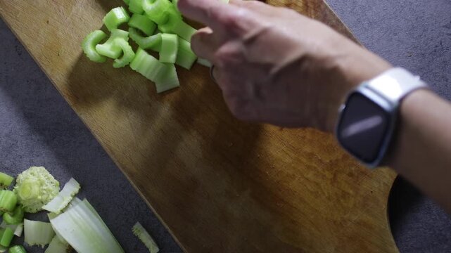 Top down view of woman hand cutting celery stalks on cutting board. Home preparing food for cooking, lifestyle