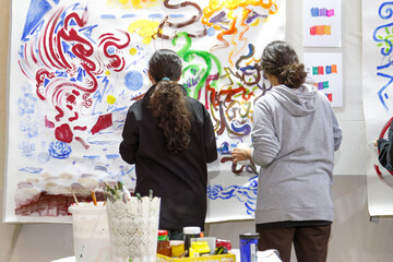 Two students painting large colorful artwork together in studio © Olga Mukashev