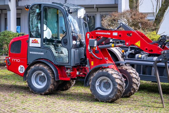 Red Weidemann 1770 CX 50 compact wheel loader with fork attachment, Specialized construction and landscaping machinery operation in tight urban environments, European-engineered machinery solution