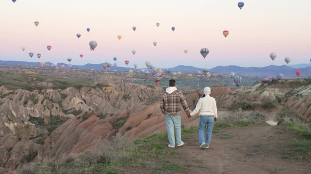 Couples explore the stunning terrain of Cappadocia while colorful hot air balloons fill the sky at sunrise. This enchanting moment showcases Turkeys unique natural beauty and romantic atmosphere.