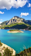 Obraz premium Serene turquoise lake surrounded by lush green mountains under a partly cloudy, bright blue sky