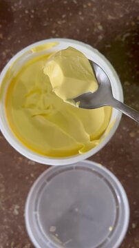 Close up of spoon scooping yellow margarine from plastic tub